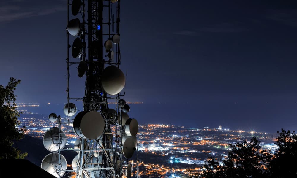 a satellite tower in front of a city landscape at night